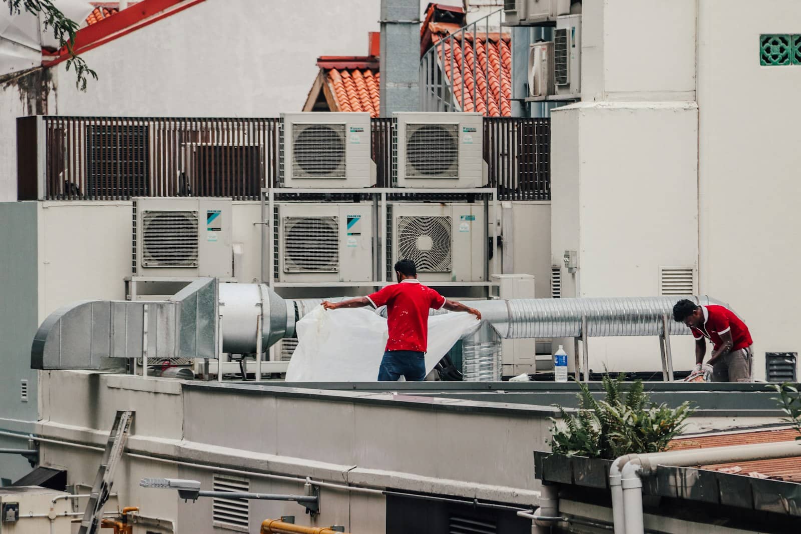 Two technicians working on rooftop condenser units and spiral duct