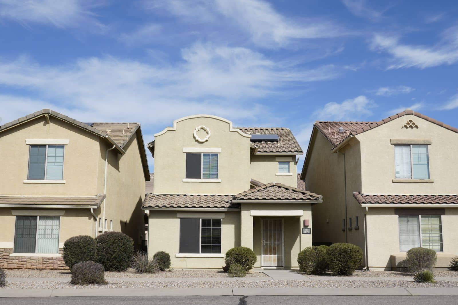 Row of Southwestern stucco homes with tile roofs and gravel desert landscaping under a clear sky