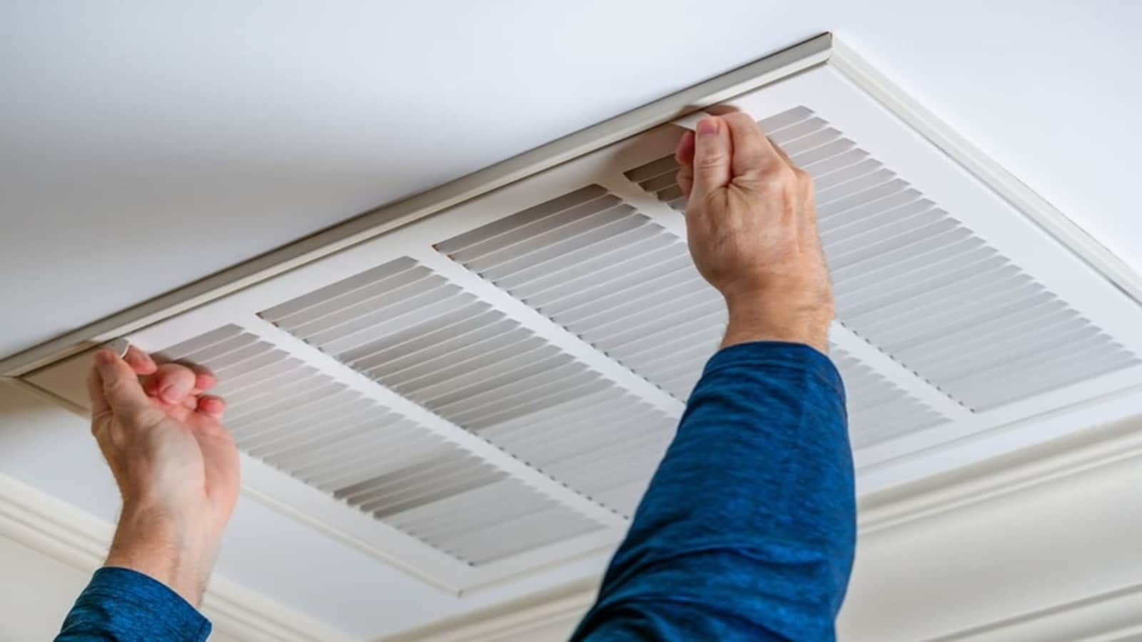 Hands opening a ceiling return-air grille to change the filter