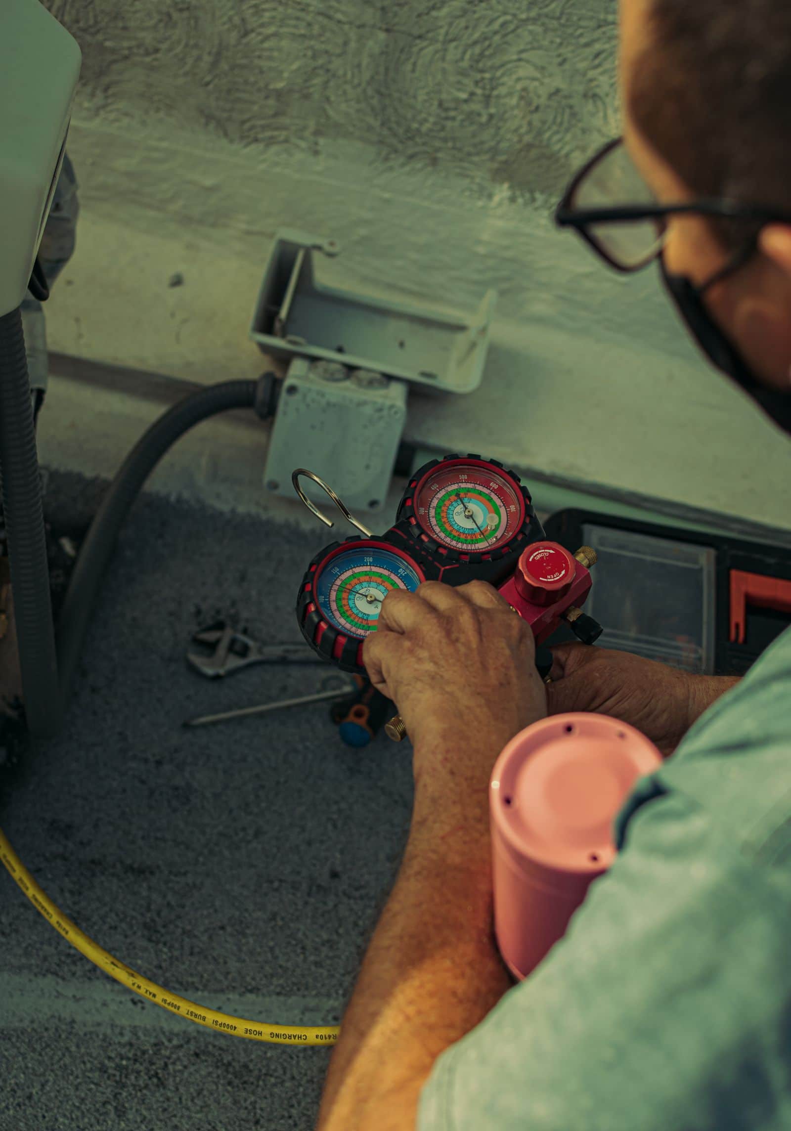 Refrigeration manifold gauges in a technician's hand during a charge check at a condenser