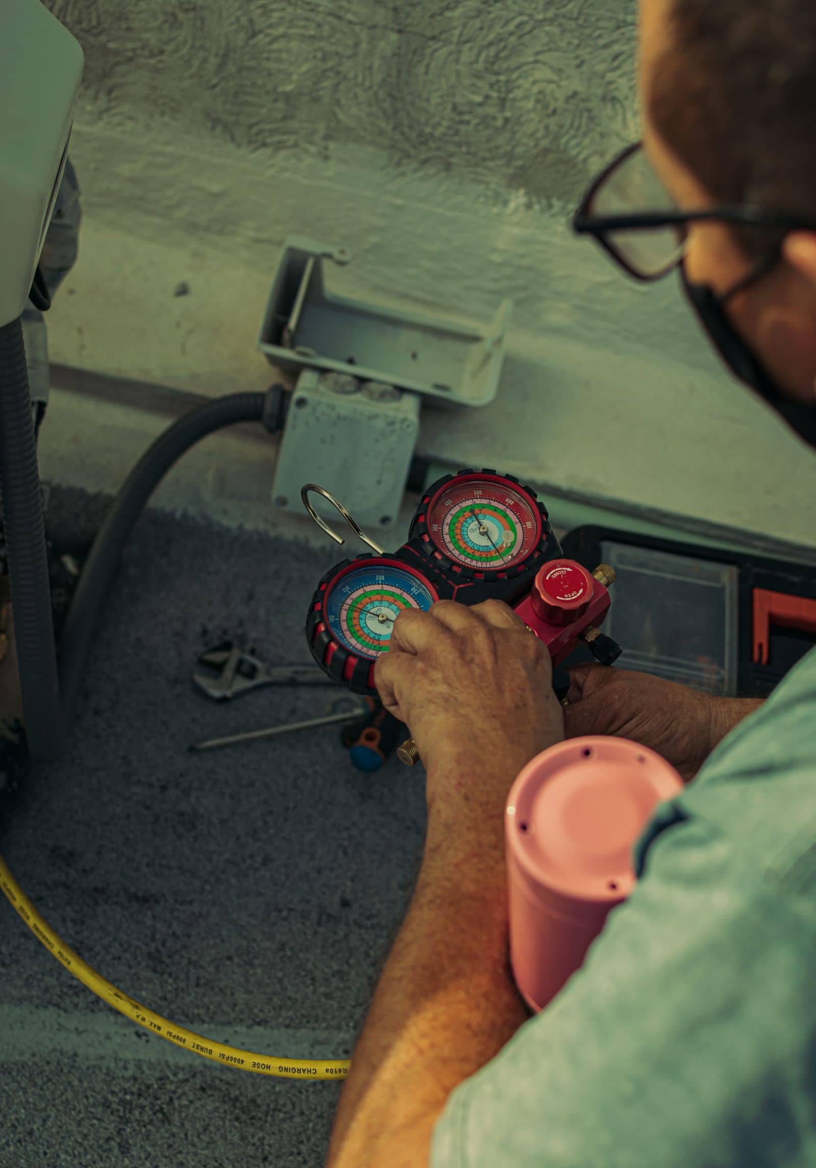 Refrigeration manifold gauges in a technician's hand during a charge check at a condenser
